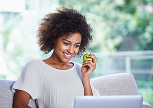 Lady Smiling at Computer While Holding a Green Apple